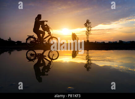 Reflet Silhouette de mère avec son enfant sur vélo contre le coucher du soleil et des reflets. L'activité de la famille asiatique de vie. Banque D'Images