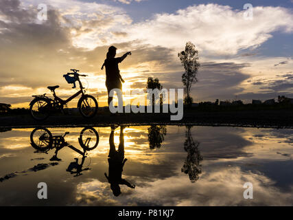 Reflet Silhouette de mère avec son enfant contre le coucher du soleil et vélo. L'activité de la famille asiatique de vie. Banque D'Images