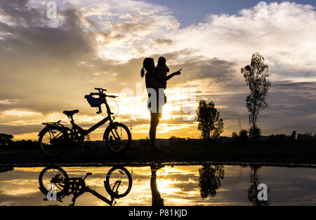 Reflet Silhouette de mère avec son enfant contre le coucher du soleil et vélo. L'activité de la famille asiatique de vie. Banque D'Images