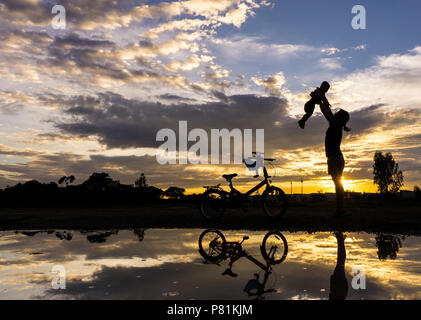 Reflet Silhouette de mère avec son enfant contre le coucher du soleil et vélo. L'activité de la famille asiatique de vie. Banque D'Images