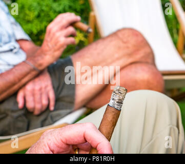 Close up of senior man sitting in transats dans un jardin d'été profiter de fumer un cigare cubain, London, England, UK Banque D'Images