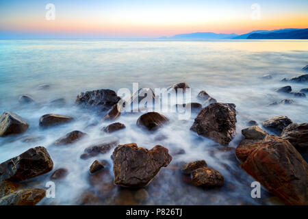 Atmosphère romantique dans la matinée en mer. Gros rochers qui sortent de la mer ondulée lisse. Horizon rose avec premier rayons de soleil chaud. Banque D'Images