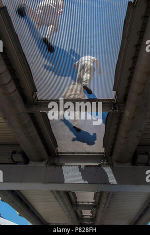 Les piétons marcher sur le pont du Millenium, vu d'en bas, à travers la grille transparente Banque D'Images