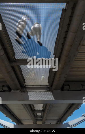 Les piétons marcher sur le pont du Millenium, vu d'en bas, à travers la grille transparente Banque D'Images