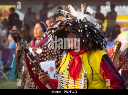 Une ancienne Native American man dans un pow-wow avec une coiffure de plumes et vêtement jaune et rouge qu'il porte un drapeau avec une tête d'aigle. Banque D'Images