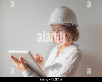 Belle asiatique ingénieur femme cheveux courts bouclés vêtu de blanc casque de sécurité et une chemise blanche avec de l'argent de travail comprimé et souriant. Femme au travail conc Banque D'Images