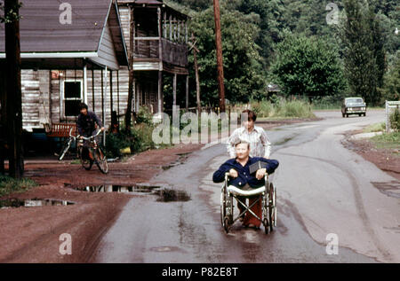 Jack Smith, 42, mobilité Miner à Rhodell, WV, à roues est dans la rue par sa fille, 16 ans, à la barre qu'il opère. Il a travaillé dans les mines un an lorsque ses jambes furent écrasés. 1974 Banque D'Images