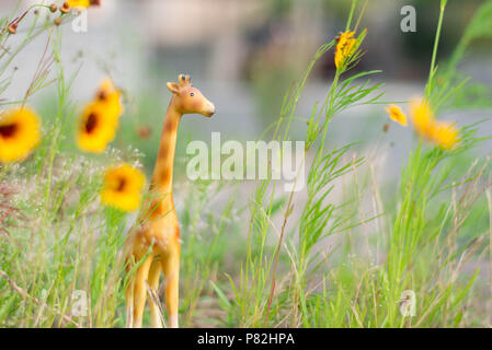 Figurine girafe miniature dans l'herbe et fleurs jaune comme un mini-safari. Banque D'Images