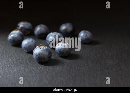 Groupe de neuf des bleuets canadiens est allongé sur une table en pierre sombre. Tout est sur un fond sombre. Banque D'Images