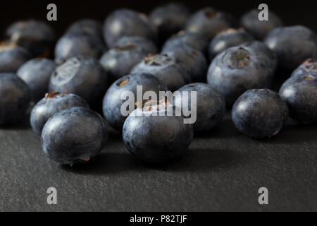 Groupe des bleuets canadiens frais est allongé sur une table en pierre sombre. Tout est sur un fond sombre. Banque D'Images