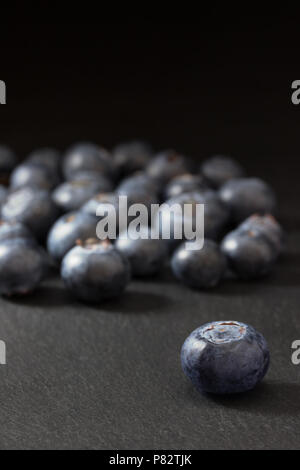 Photo verticale de l'un Canadien blueberry debout devant le groupe des bleuets est posé sur une table en pierre sombre. Tout est sur une zone sombre Banque D'Images