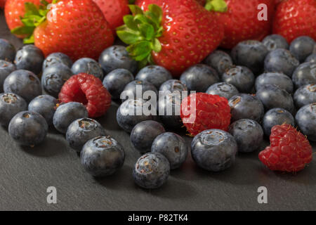 Mélange de fraises, bleuets et framboises est allongé sur une table en pierre sombre. Banque D'Images