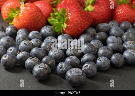 Vue depuis l'angle d'un mélange de fraises et de bleuets allongé sur une table en pierre sombre. Banque D'Images