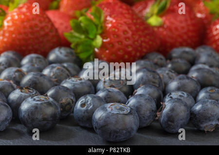 Mélange de fraises et de bleuets allongé sur une table en pierre sombre. L'accent sur les bleuets au premier plan. Banque D'Images