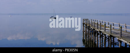 Vue panoramique sur Strangford Lough en été mist et réflexions des nuages clairs et bateaux à l'horizon. Une jetée en bois cadres la photo. Banque D'Images