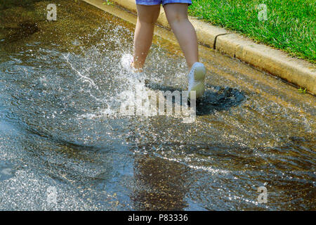 Fille enfant heureux jour pluvieux de courir et sauter dans les flaques d'eau après la pluie en été voir les gouttelettes d'eau Banque D'Images