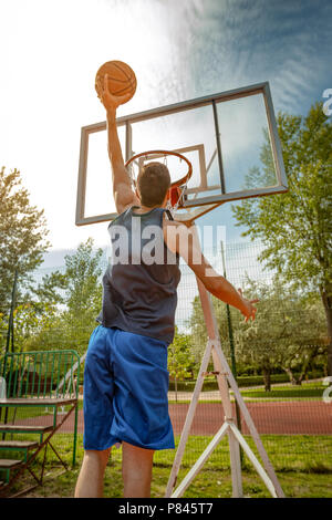 Jeune joueur de basket-ball de rue montrant ses compétences sur cour. Il jette dunk. Banque D'Images