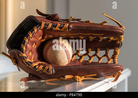 Close-up of a utilisé le baseball ball à l'intérieur en cuir brun, un gant de baseball dans un fond gris. Banque D'Images