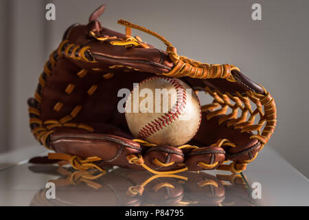 Close-up of a utilisé le baseball ball à l'intérieur en cuir brun, un gant de baseball dans un fond gris. Banque D'Images