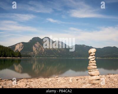 Pierre pyramide équilibrée sur le rivage de l'eau bleu de lac de montagne. Les montagnes bleues du niveau de l'eau miroir. Banque D'Images