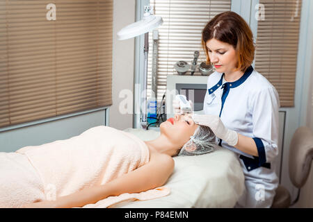 Photo de nice coiffeur faisant une oxygénothérapie pour jeune femme fixant les yeux fermés dans un salon de beauté. Banque D'Images