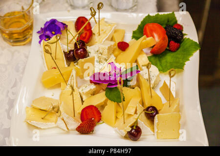 Assortiment de fromages sur une plaque carrée, morceaux de fromage et de fromage Brie, fraises et cerises Banque D'Images