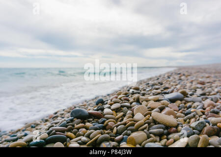 Cailloux humides situées sur la plage près de la mer ondulant par jour nuageux. Banque D'Images