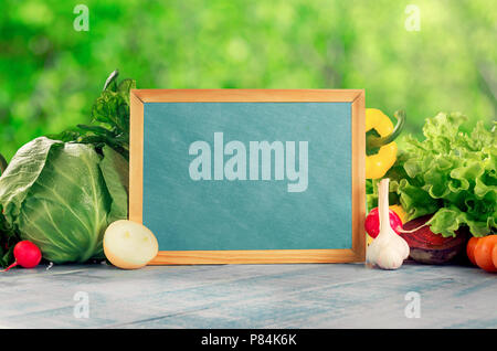 Tableau sur lequel un ensemble de différents légumes frais sur la table en bois bleu contre feuilles vert en arrière-plan flou Banque D'Images