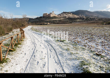 Sur assise ville (Ombrie) en hiver, avec une route de campagne couverte de neige et un ciel bleu avec des nuages blancs Banque D'Images