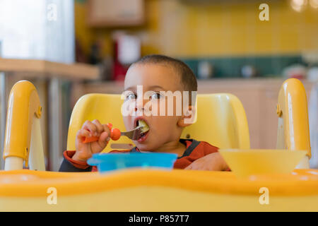 Le garçon 2 ans à manger de la viande. Table enfant. Le concept de l'indépendance de l'enfant. funny enfant dans un siège bébé Banque D'Images