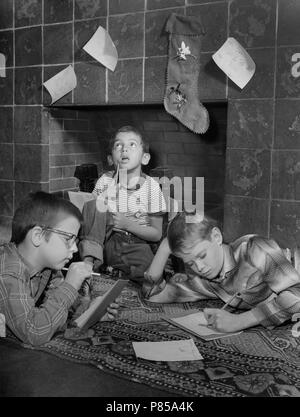 Les enfants écrivent des lettres au Père Noël en face de leurs bas accrochés avec soin sur la cheminée, ca. 1959. Banque D'Images