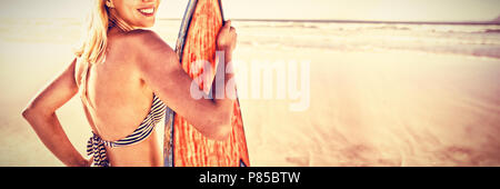 Portrait of smiling woman holding surfboard at beach Banque D'Images