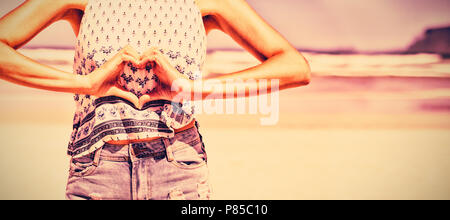 Mid section of woman making heart shape with hands at beach Banque D'Images