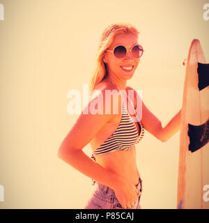 Portrait of smiling young woman holding surfboard at beach Banque D'Images