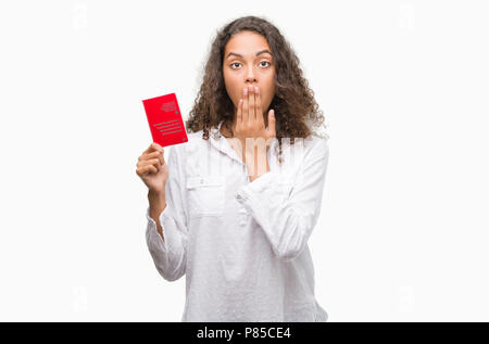 Young hispanic woman holding passport de Suisse couvrir la bouche à part choqué avec honte pour erreur, expression de la peur, peur en silence, secr Banque D'Images