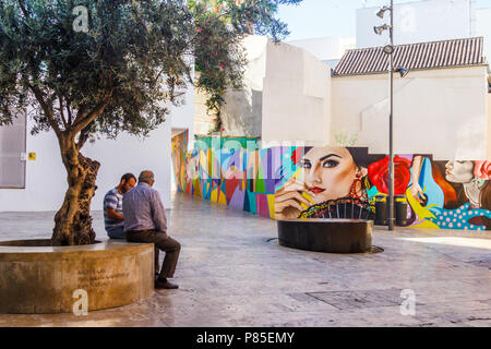 Malaga, Espagne 18 Juin 2018 : deux hommes assis à parler en petit carré avec wall mural. La murale est typiquement espagnol Banque D'Images