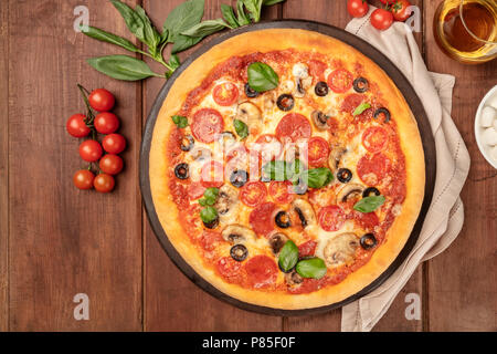 Photo prise à la verticale de la pizza au pepperoni, avec verre de vin blanc, tomates cerises et feuilles de basilic frais, tourné à partir de ci-dessus sur fond rustique foncé avec pla Banque D'Images