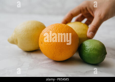 Mélange de fruits ou agrumes orange, citron et lime sur la table. A woman's hand prend un citron. Banque D'Images