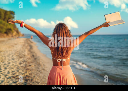 Vue arrière d'une belle jeune femme jouissant sur la plage avec des adresses de son bras ouverts. Banque D'Images