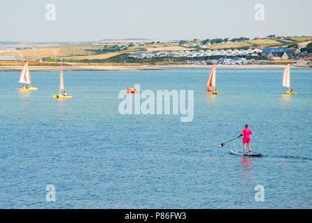 Le Dorset. 9e juillet 2018. Une femme-paddle boards à sunny Portland port en tant qu'écoliers apprendre à naviguer Crédit : Stuart fretwell/Alamy Live News Banque D'Images