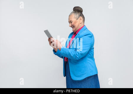 Voir le profil de man holding et à la recherche à l'écran avec visage satisfait et souriant à pleines dents. Grand-mère en costume bleu avec des cheveux gris bun ha Banque D'Images