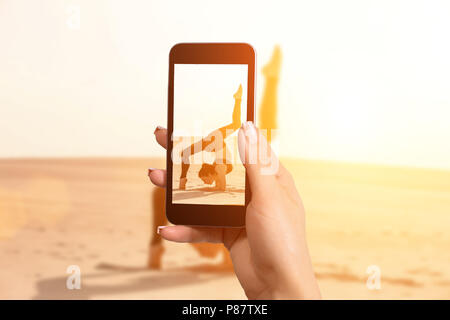 Femme de prendre une photo avec votre téléphone mobile une femme faisant un stunt acrobatique sur le sable Banque D'Images