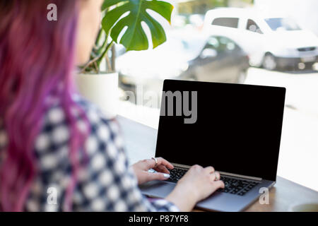 Vue arrière d'une jeune femme cheveux rose sur un clavier d'ordinateur portable avec écran espace copie vierge tout en étant assis dans le café. Banque D'Images