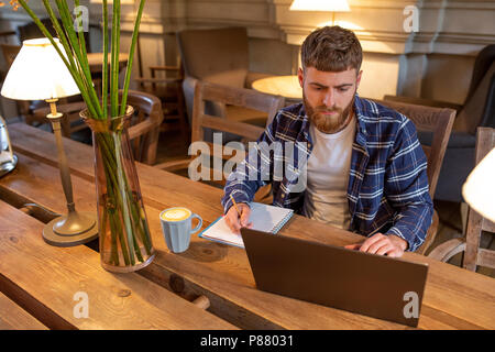 L'homme d'affaires occasionnels ou indépendant de son travail sur la planification de travail sur ordinateur portable, ordinateur portable avec smart phone, tasse de café sur la table à café ou bureau à domicile. Banque D'Images