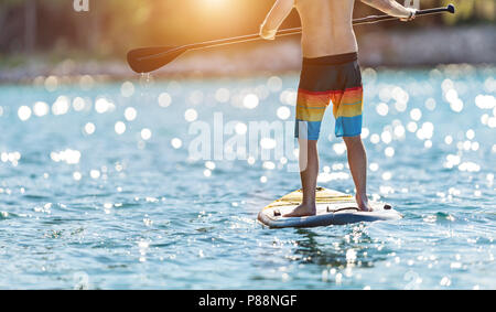 Détail de jeune homme debout sur le paddleboard. Paddleboarding est le moyen moderne de transport l'activité de l'eau et le sport. Banque D'Images