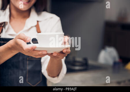 Asie femme porter un tablier barista jean holding Coffee cup chaud servi au client avec smiling face au comptoir du bar, café restaurant service concept.serveuse Banque D'Images