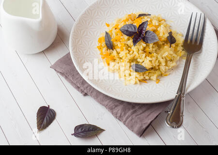 Pilaf traditionnel, riz aux légumes et basilic frais dans une assiette sur une table en bois clair Banque D'Images