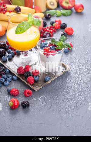 Les différentes baies et fruits sur un fond gris, jus de fruits frais, yaourts et petits fruits pour le petit déjeuner. Les vitamines et les aliments detox. Copy space Banque D'Images