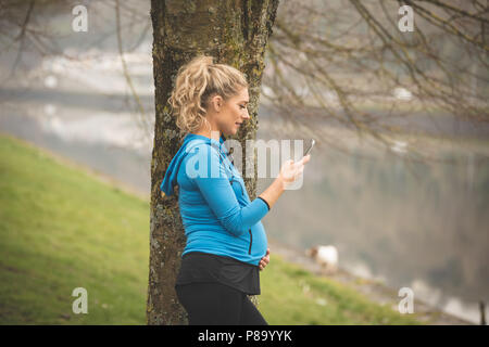 Femme enceinte à l'aide de téléphone mobile dans le parc Banque D'Images