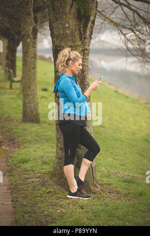 Femme enceinte à l'aide de téléphone mobile dans le parc Banque D'Images